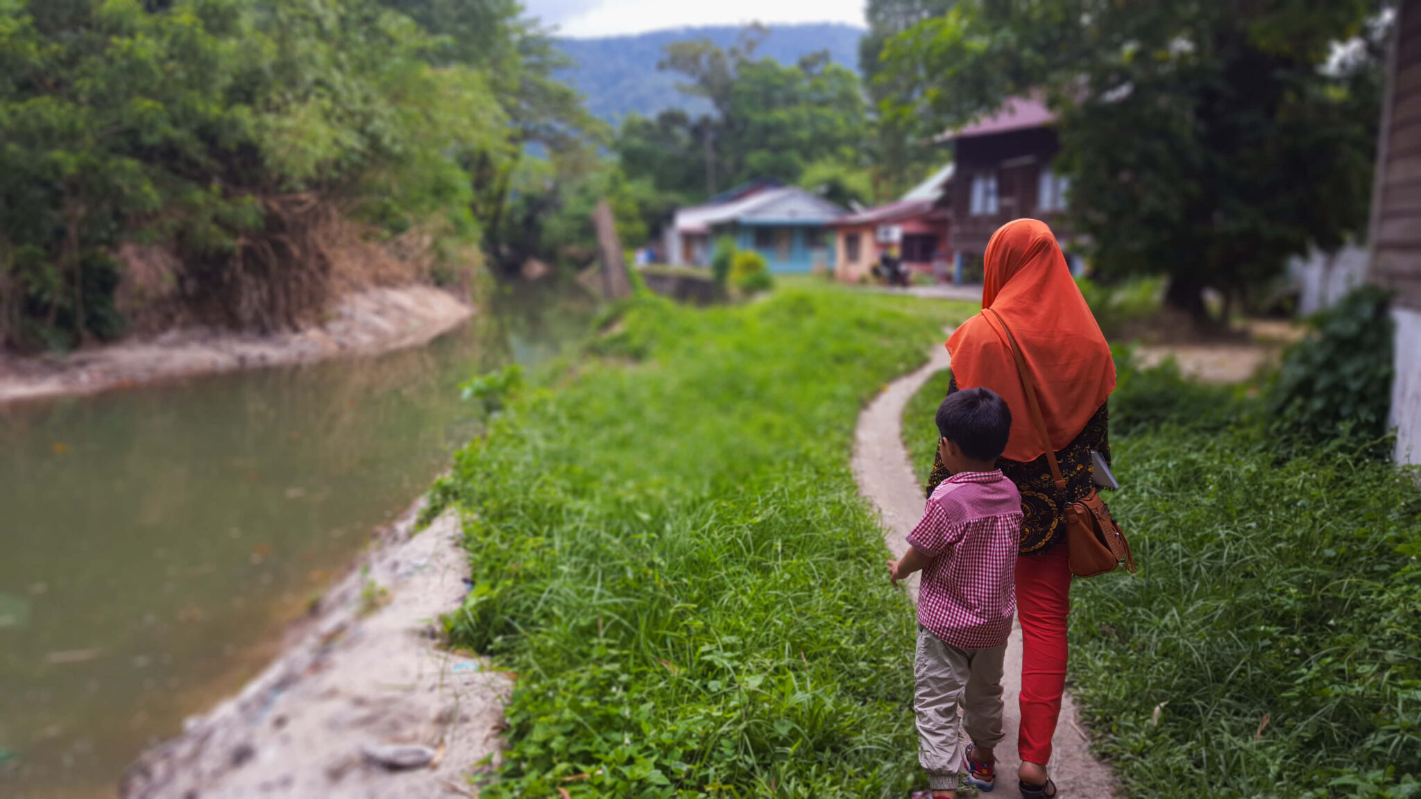 A woman and child walking to a village along a dirt path.