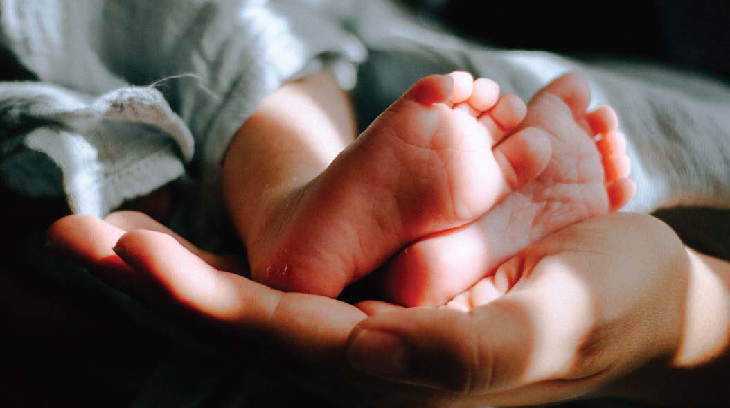A hand is gently cradling a new born baby's feet.